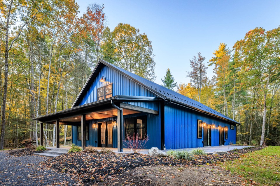 Blue barndominium home with covered porch and warm exterior lighting