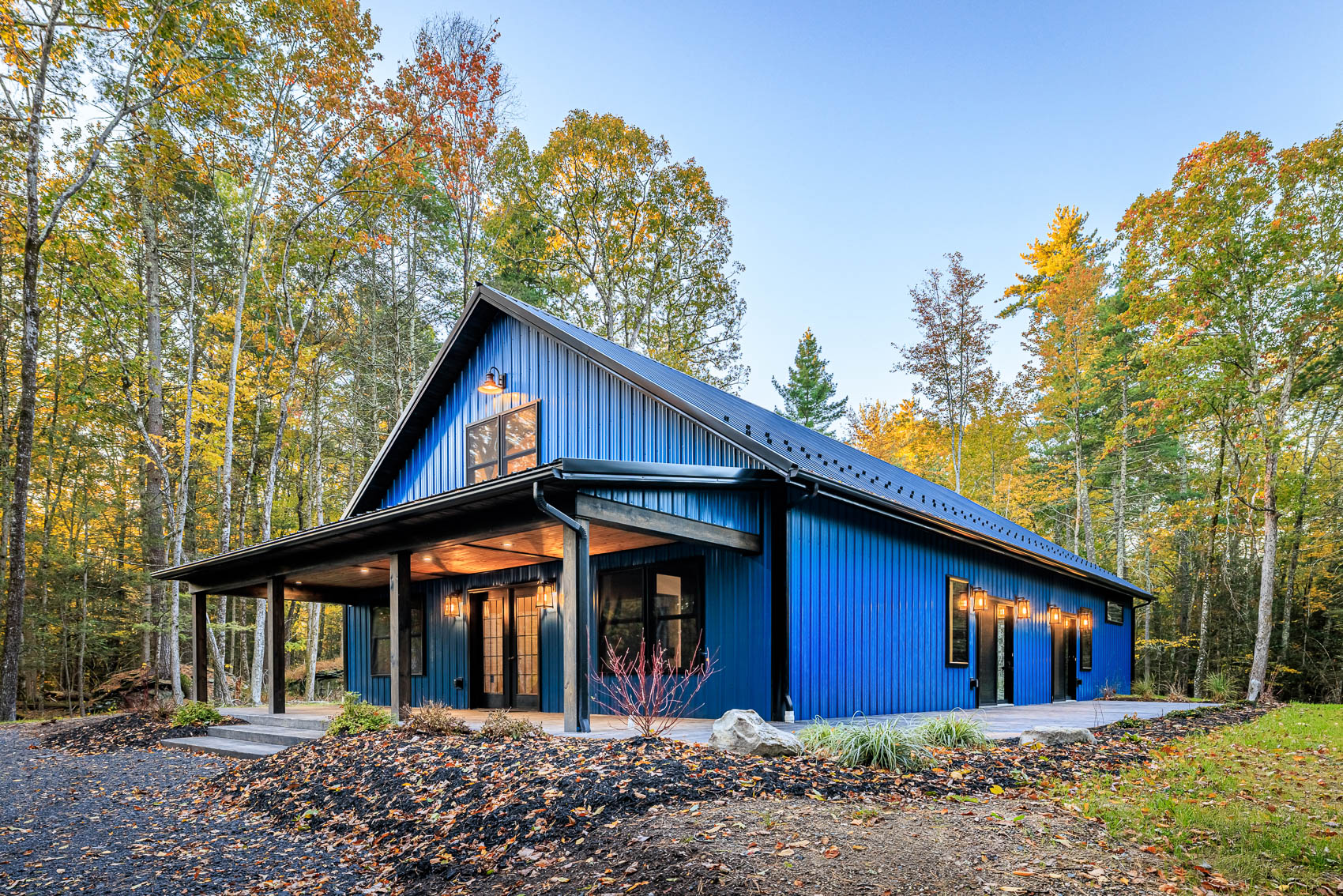 Blue barndominium home with covered porch and warm exterior lighting