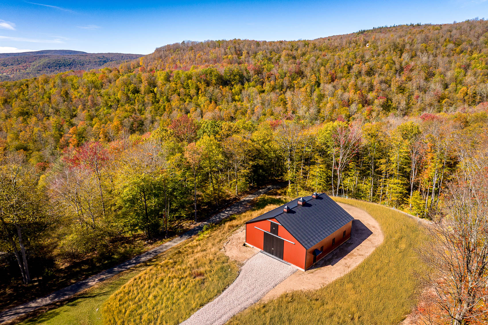 Aerial view of red post-frame barn in a wooded hillside setting
