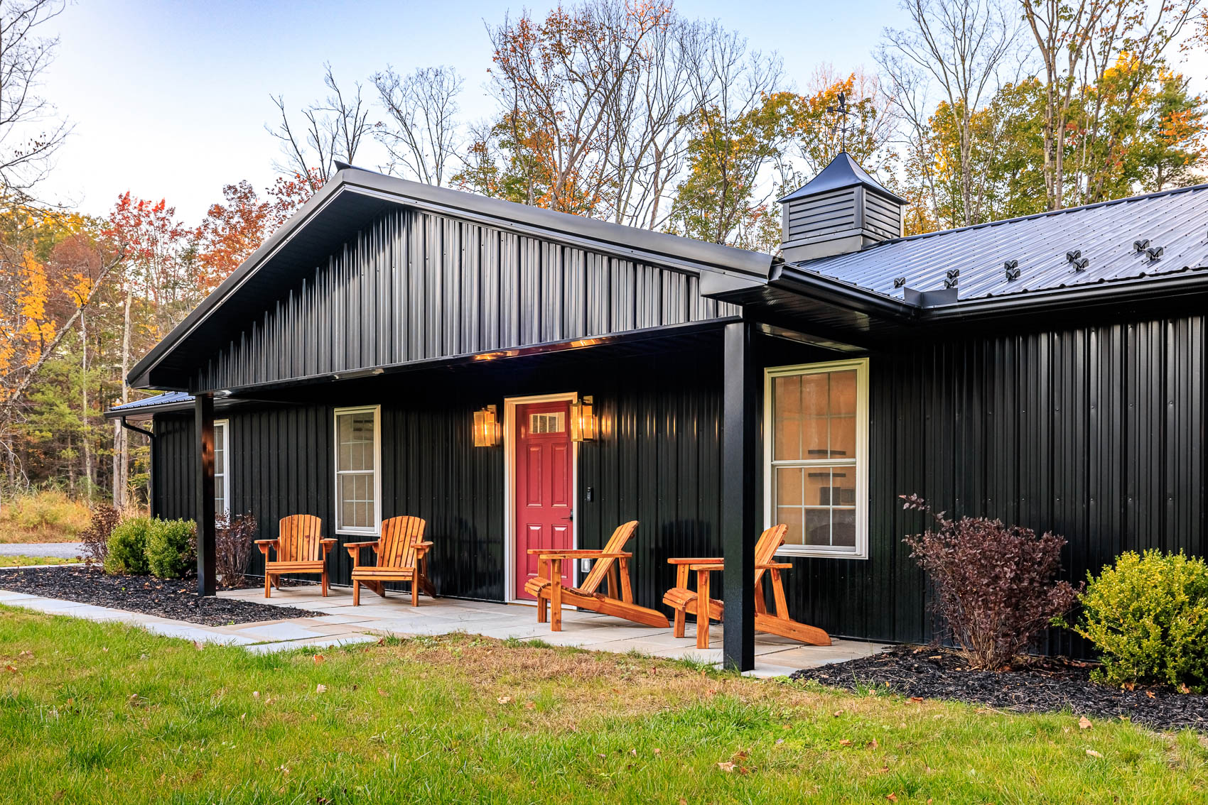 Black barndominium porch with red front door, warm lighting, and seating