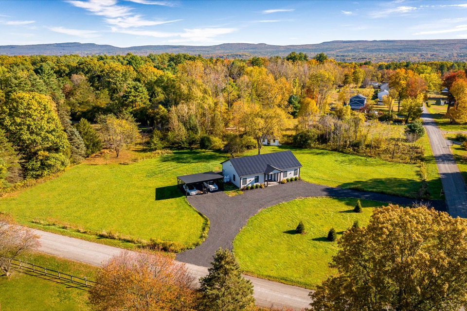 Wide aerial view of white barndominium home on open acreage